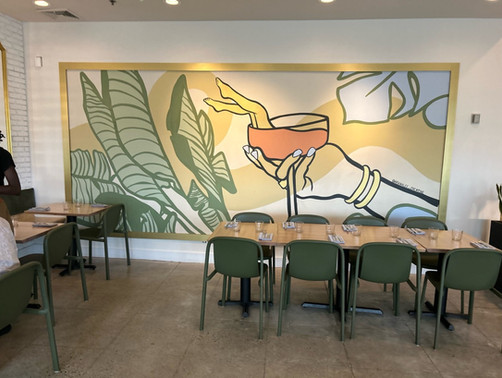 Colorful mural at Nosh and Grog of a woman holding a cocktail. Cocktail bar mural with leaves, nature, and whimsy.
