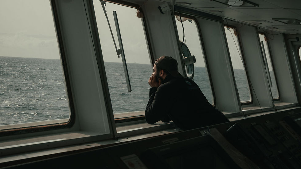 Man resting his head on his hands while looking out the window on a dark ship bridge