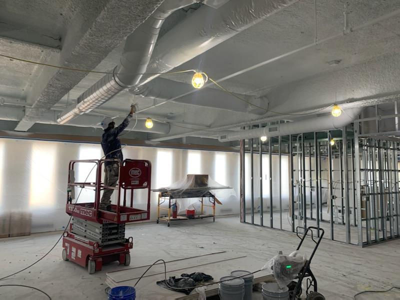 Painter on lift spraying ceiling white during commercial building renovation