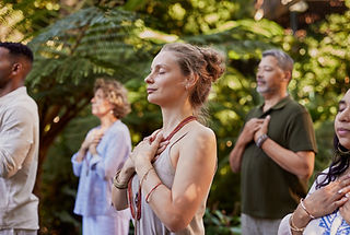 Group of people standing outdoors with hands on their hearts, practicing mindfulness in a