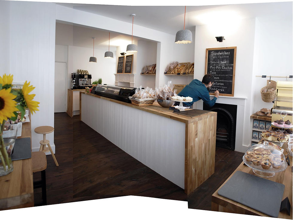 inside the Norfolk St. Bakery, a woman writes specials on a chalkboard behind a long counter full of pastries