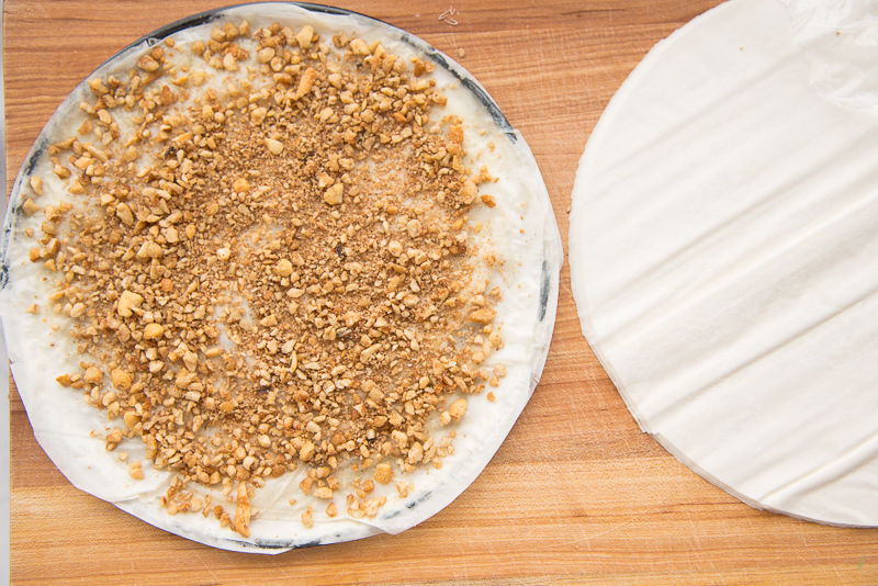 a round of phyllo dough sprinkled with chopped nuts next to a stack of phyllo dough rounds