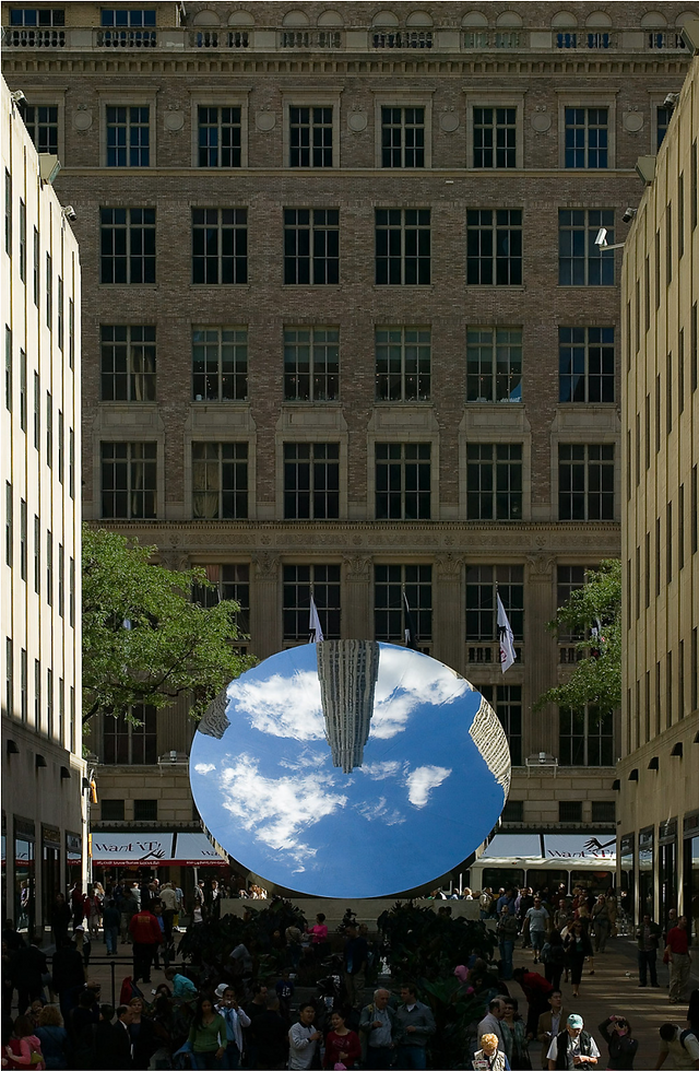 a large round mirror in the courtyard of skyscrapers reflects the sky