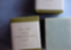 square soaps wrapped in olive green paper and brown cardstock wrappers on a periwinkle background