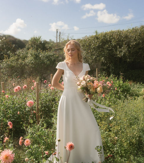 Discover Flora by Sophie Rose Bridal, a romantic wedding dress perfect for garden, countryside and outdoor weddings. Featuring a wide V neckline, delicate capped puff sleeves, floral appliqué and a button-detailed V-back, its flowing half-circle skirt completes the look. Handcrafted to your measurements in Hampshire.