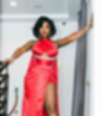 Ghanaian musician Efya in a red dress with rhinestone details poses confidently on a staircase. Modern interior with gray curtains in the background.