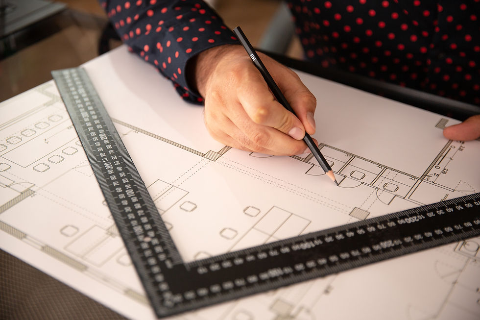 Hand in polka-dot sleeve drawing on architectural plan with a pencil, next to a black ruler on a desk.