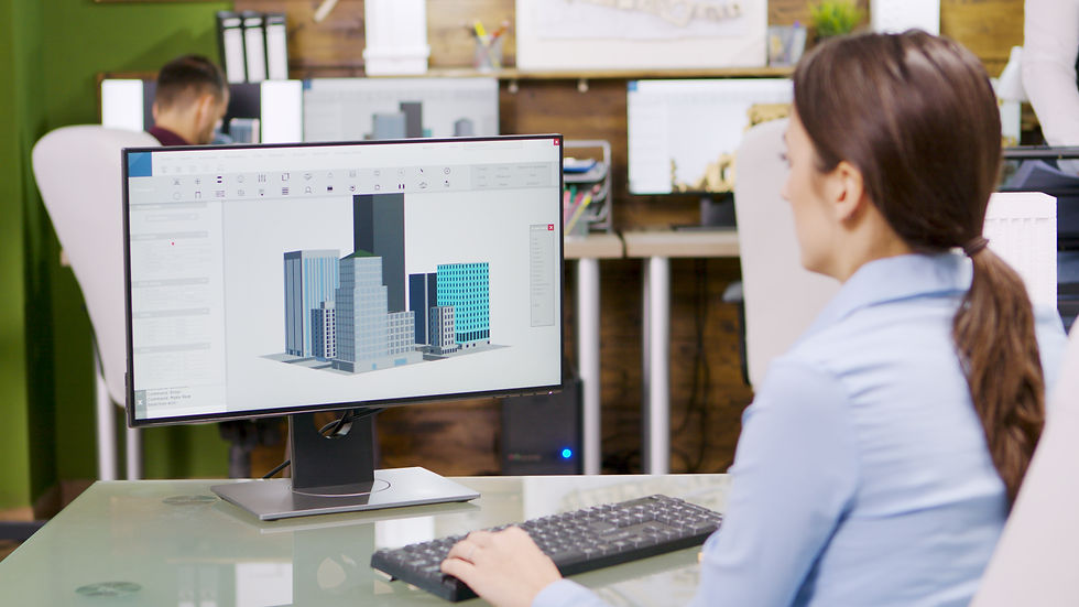 Woman at a desk works on architectural design software showing buildings on a monitor. Office setting with green walls and colleagues.