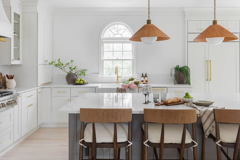 Main kitchen at Project Simpson, Marietta, GA, featuring crisp white cabinetry, pebble-gray island, sculptural plaster hood, integrated appliances, brass hardware, and rattan pendant lighting for an organic modern, elevated family home design.