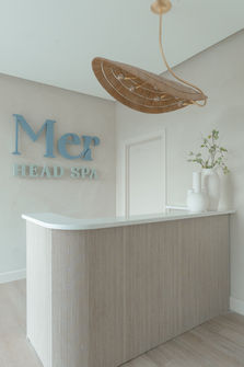 Reception desk at Project RRR with chandelier pendant light and illuminated 'Mer Head Spa' sign, styled to create a welcoming, luxurious, and calming atmosphere.