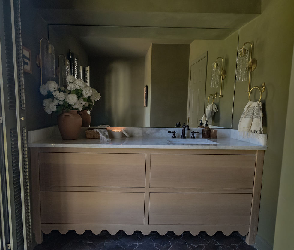 Powder room with light wood vanity, white countertop, and large mirror. Terracotta vases with white flowers; candle lit. Olive green walls.