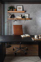 Office space at Project Manay featuring leather desk chair, black desk, dark limewash walls, and floating shelves displaying books and decorative items.