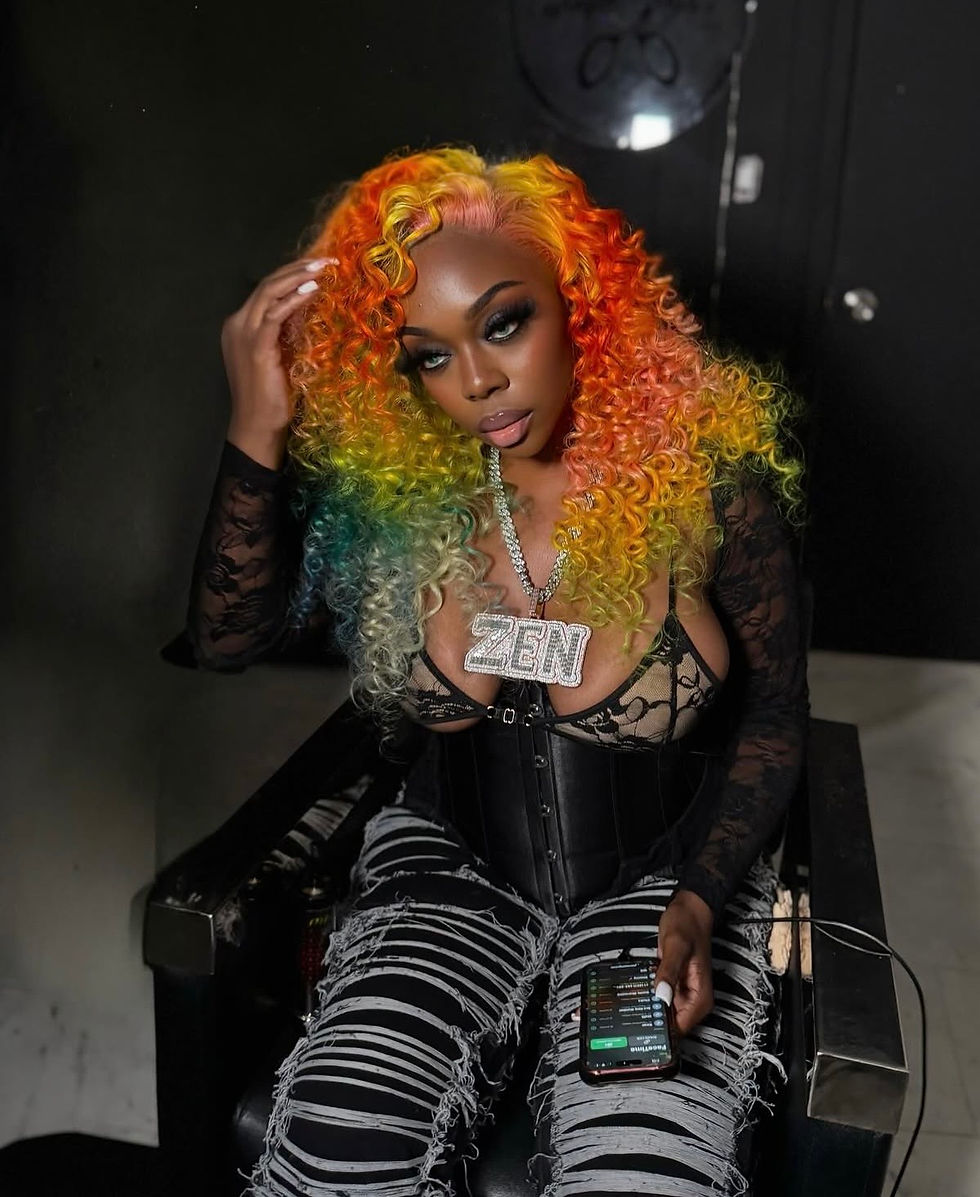 Queens rapper Big Zen radiates confidence and style, flaunting vibrant rainbow curls and a bold "ZEN" chain, all while effortlessly holding a phone.