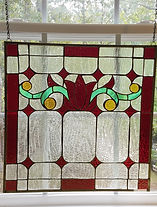 Square stained-glass piece featuring geometric shapes in yellow, green, and red intermixed with frosted glass panels. 