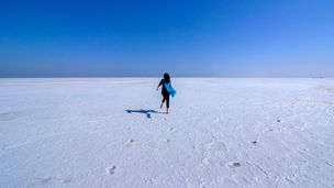 a woman in a blue scarf is walking across a salt marsh