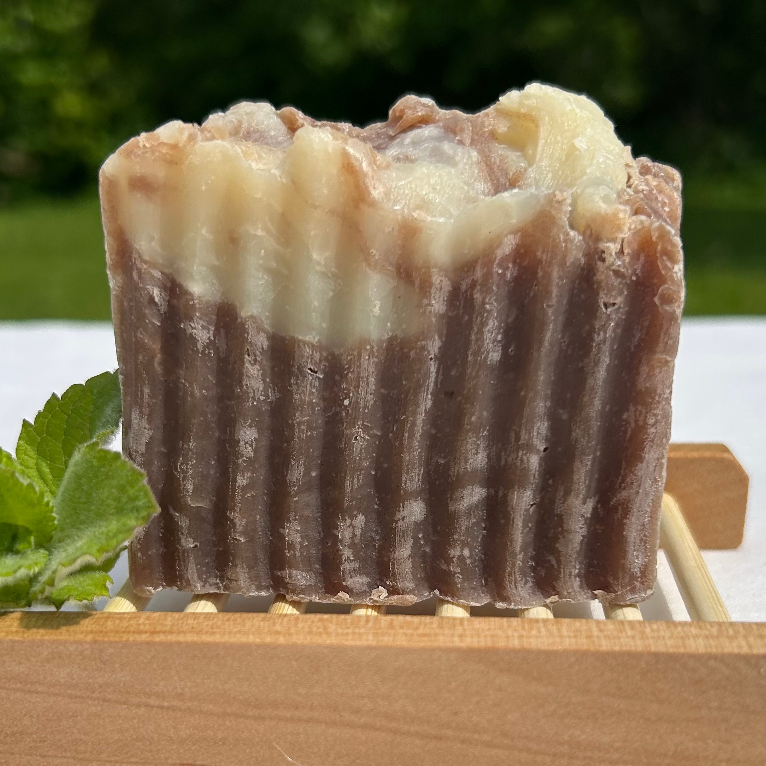 Handcrafted chocolate mint soap with coconut milk, topped with a dusting of cocoa and styled with fresh mint leaves on a rust