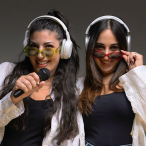 two girls holding mics and wearing headphones doing a photoshoot for a podcast