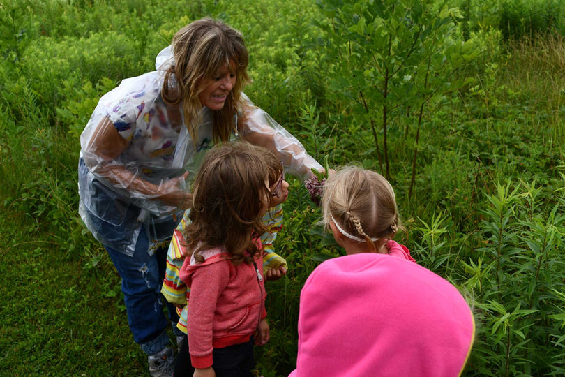 A woman shows children a flower in a forest preserve.