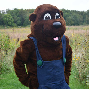A woodchuck mascot poses for a photo in a prairie.