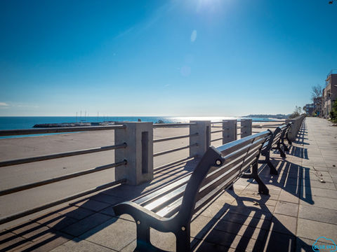 A sandy beach with a promenade and benches, with the sun shining brightly.