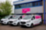 Three white vans with "Liftability" branding parked outside an industrial building with a pink sign. A tree is visible nearby.