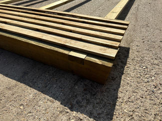 Partially assembled featheredge fence panel showing notched timber posts, three horizontal rails, and vertical featheredge boards laid out on concrete.