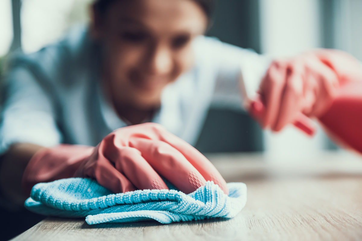 A cleaner wearing pink rubber gloves thoroughly wipes down a wooden surface with a blue cloth, ensuring a spotless finish.