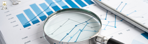 Magnifying glass over blue bar and line graphs on paper, with pen beside it. The text shows month names, suggesting data analysis.