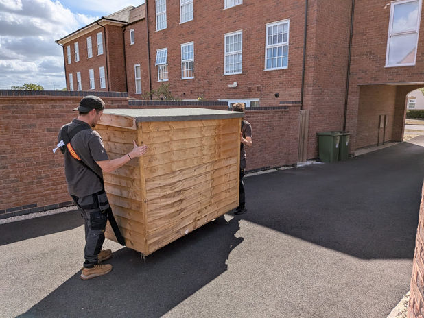 Removal team carrying heavy garden storage box using shoulder straps during New Lubbesthorpe move.
