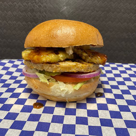 Delicious burger with layers of vegetables on a checkered blue and white surface.