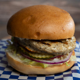 Delicious burger with fresh toppings on a checkered napkin, wooden background.