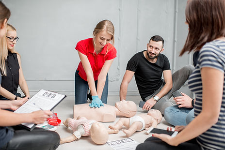Group of adults taking part in a first aid training session with CPR practice on a resuscitation manikin.