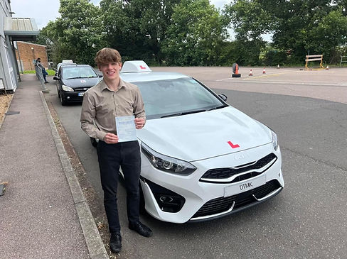 Learner driver holding practical driving test pass certificate beside DTMK Driving School Kia Ceed with L plates in Milton Keynes.