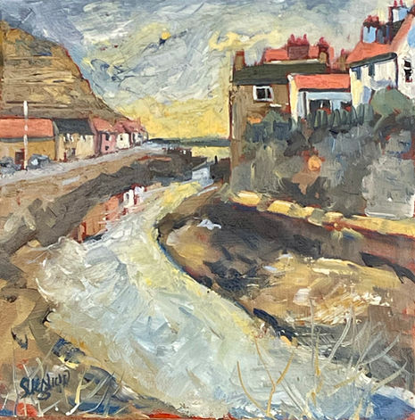 A golden sky is reflected in Staithes beck in a tranquil coastal scene.