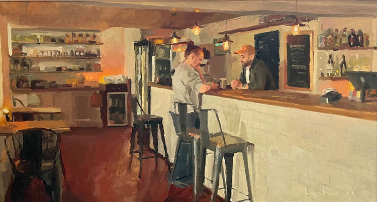 A cozy interior view looking along the white and wooden serving counter of Mary’s cafe illuminated by glowing light bulbs.
