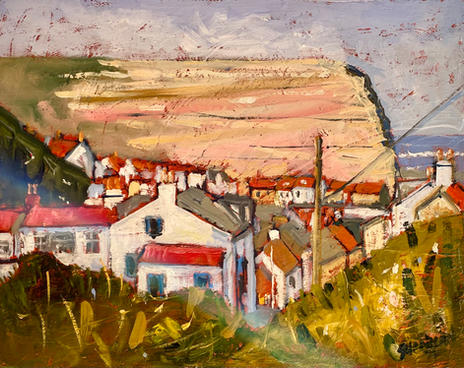 A view of closely huddled terracotta roofed cottages glimpsed through receding hedgerows with the sunlit Cowbar cliff face in the background.