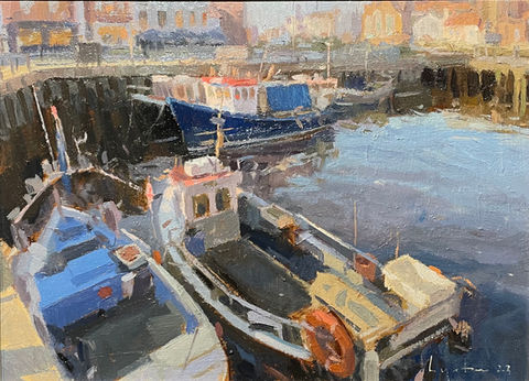 A view from Whitby quayside looking down onto the fishing boats moored up- on the other side of the blue water are views of Whitby Old Town.