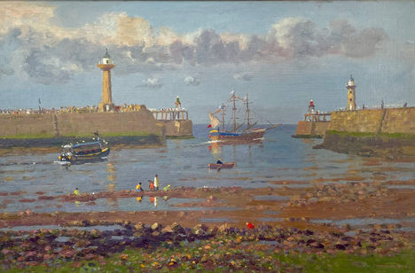 A breezy summer’s day looking down over the sand, sea and piers of Whitby harbour. Pleasure craft including the miniature Endeavour float in the water.