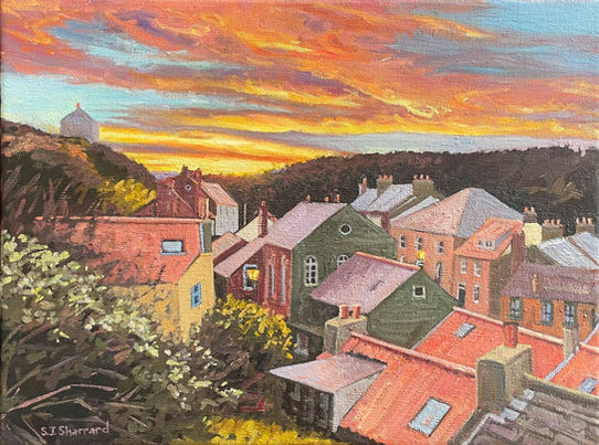 A vibrant view looking down on Staithes rooftops illuminated by a dramatic sunset.