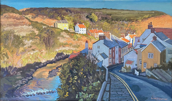 A view looking down into Staithes from the top of the High Street, with Cowbar glowing in morning sunlight and the cottages in shadow.