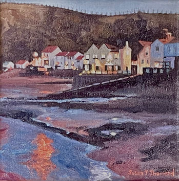 An intimate view of Staithes seafront at night: the lights reflect onto the damp sand in the foreground.