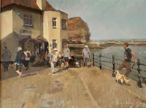 A view of the Cod and Lobster pub swathed in sunlight with Cowbar and the sea beyond. A man with a spaniel leans on railings in the foreground.