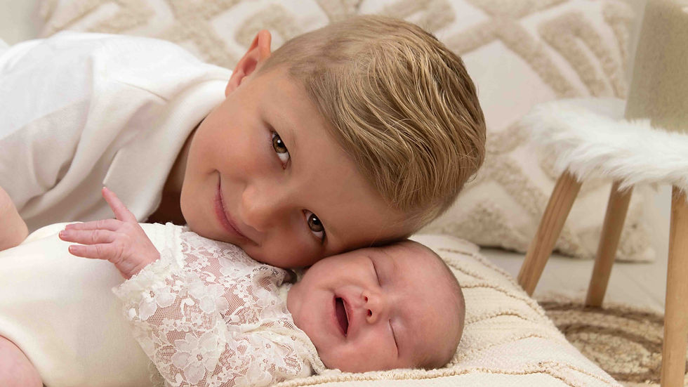 Kleiner Junge kuschelt lächelnd mit schlafendem Baby auf hellem Teppich im gemütlichen Wohnzimmer.