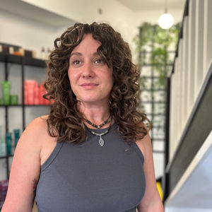 a woman with curly hair wearing a necklace with a leaf pendant