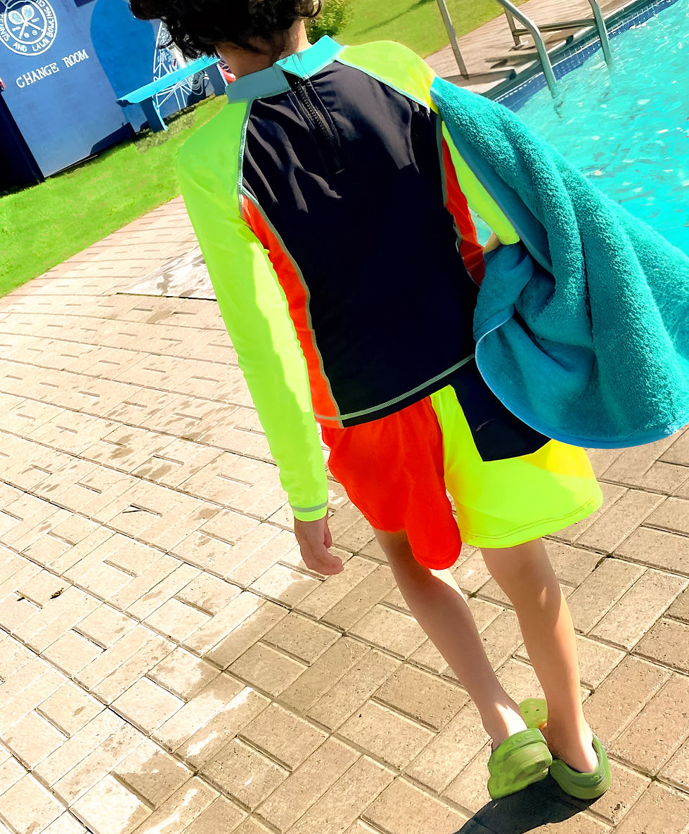 Thumbnail: A child walking poolside holding a teal towel, wearing the UPF Sun Protective Kid's Swim Top and Board Shorts w green Crocs