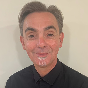 Raymand Baxter in a senior stylist in Head hair and Beauty in Gandy street, Exeter. He specializing in cutting hair. He is smartly dressed in a black shirt agaist a black background in the salon.