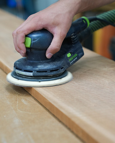 Sanding a handcrafted wooden pivot trivet for a smooth, durable finish before final inspection.