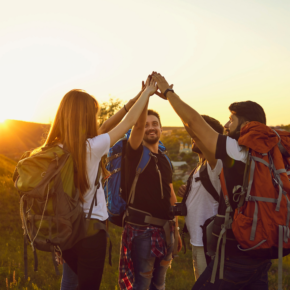 A group of hikers celebrates reaching the summit with a high-five at sunset, showcasing teamwork and adventure against a stunning landscape.