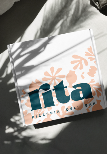Branded Rita pizza box, placed in soft dappled sunlight on white surface.