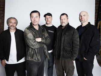 Fotografía promocional en plano medio de los cinco integrantes de la banda de rock alternativo Faith No More, posando juntos de pie sobre un fondo blanco de estudio